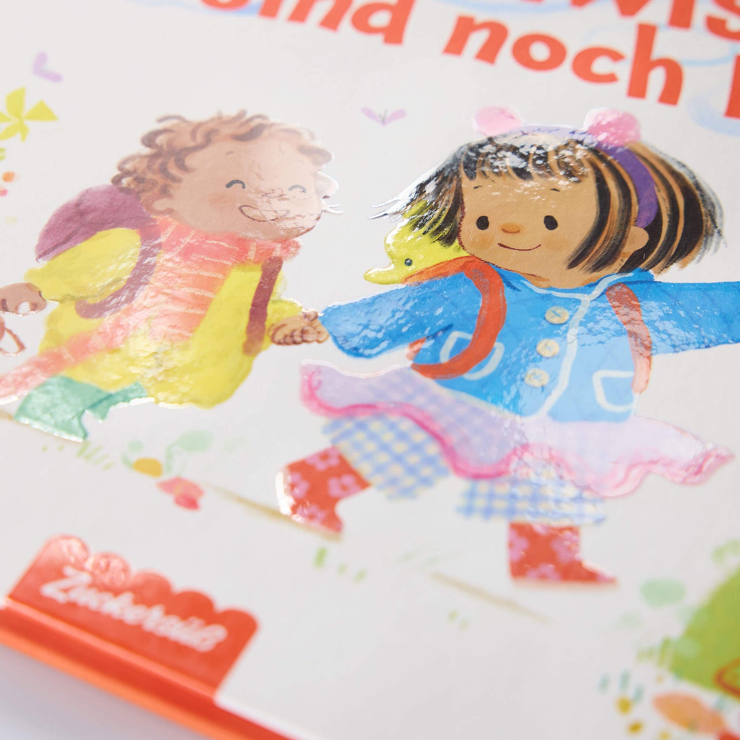 Umschlagillustration von zwei lächelnden Kindern in bunter Kleidung mit Rucksäcken, die sich an den Händen halten. Der Buchtitel "Auch große Geschwister sind noch klein" und das rote Logo des Zuckersüß Verlags sind teilweise sichtbar.